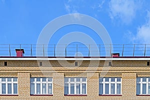 Brick facade of the house with a roof and white windows against the blue sky.