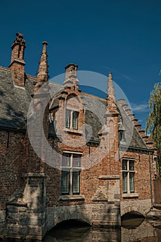 Brick facade of old house over water and trees in a sunny day, at park of Bruges.