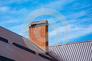 Brick forged chimney on roof of house in the sunlight. Clear blue sky background