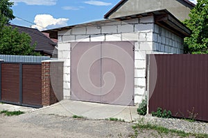 brick garage with brown gates and metal fence on the street by the road