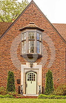 Brick house with bay window centered above the arched marble tiled door with statues of greyhoud dogs flanking the prorch - photo