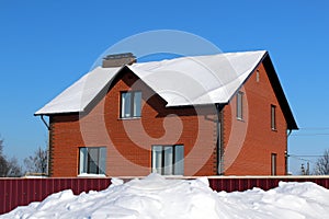 A brick house stands in winter under the snow on a bright frosty day