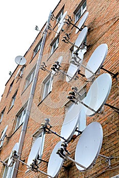 Brick house on the wall of which is attached a lot of satellite dishes