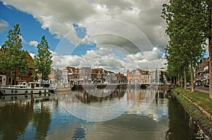 Brick houses, moored boats and bascule bridge reflected in wide canal water surface on sunset in Weesp.