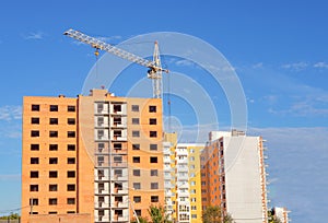 Brick multistory building under construction with crane on the site, new condominium on background