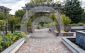 The brick path of a well manicured sensory garden lined by plants and a fountain.