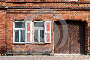 Brick structure features red shutters and a wooden door, set against a clear sky backdrop. photo