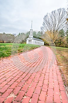 Brick walkway leading to old, white New England church in the distance