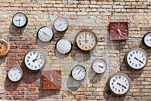 Brick wall background with numerous round and square clocks.