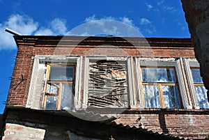 Brick wall of building with one boarded up broken window, view from top on slate roof and blue sky