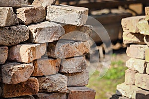 Brick wall corner with sticking out old red bricks and visible grass on the background