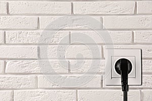 Brick wall with power socket and inserted plug, space for text. Electrical supply