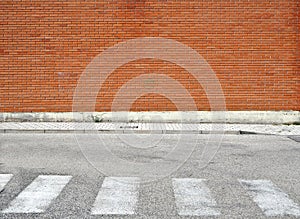 Brick wall with a sidewalk made of concrete tiles and a weathered asphalt street with crosswalk.