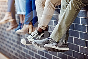 Brick wall, student feet and friends outdoor on university campus together with sneakers. Relax, urban youth and foot at