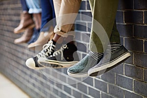 Brick wall, students feet and friends outdoor on university campus together with sneakers. Relax, youth and foot at