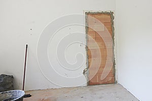 bricked up door in a living room with white walls, next to a black vat and a broom