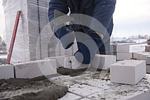 A bricklayer aligns bricks in cement, makes a concrete wall.