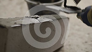 Bricklayer applies adhesive glue on autoclaved aerated concrete blocks with notched trowel and spatula. Brickwork worker