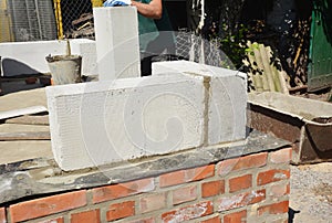 Bricklayer builder laying autoclaved aerated concrete blocks, aac on house foundation wall