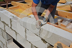Bricklayer builder laying autoclaved aerated concrete blocks for house wall near unfinished roof top