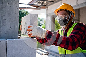 Bricklayer builder working with autoclaved aerated concrete blocks. Walling, installing bricks on construction site