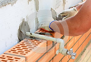 A bricklayer is building a brick exterior wall with an outdoor water faucet or hose bibb.Constructing a cavity wall with an photo