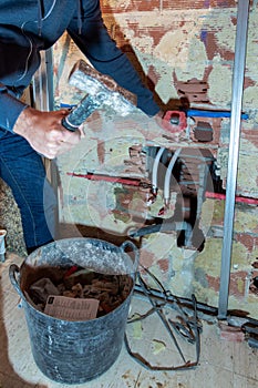 Bricklayer chipping a brick wall at a construction site to make way for the water pipes with a basket of debris