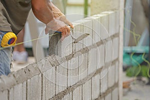 bricklayer hands hold aluminium brick trowel installing brick blocks on construction site