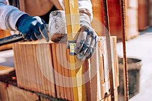 Bricklayer industrial worker installing brick masonry on exterior wall using level and rubber hammer