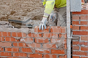 Bricklayer laying bricks on mortar on new residential house construction.