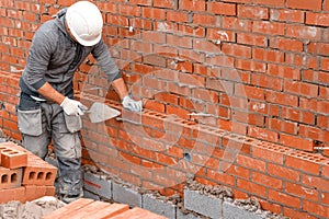 Bricklayer laying bricks on mortar on new residential house construction