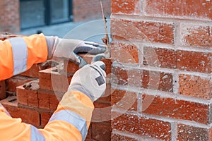 Bricklayer laying bricks on mortar on new residential house construction.