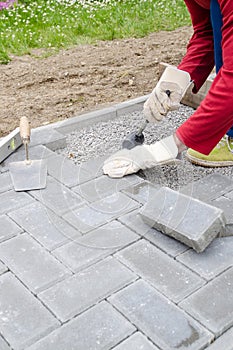 Bricklayer places concrete paving stone blocks for building up a patio, using hammer and spirit level