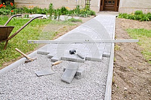 Bricklayer places concrete paving stone blocks for building up a patio, using hammer and spirit level