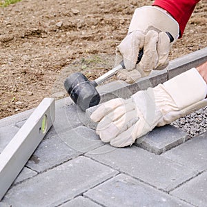 Bricklayer places concrete paving stone blocks for building up a pave patio, using hammer and spirit level. Handyman DIY concept