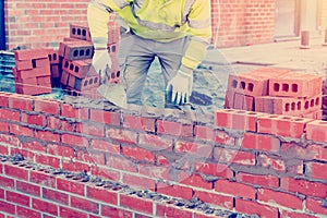 Bricklayer in safety vest and a helmet laying brick wall using a trowel