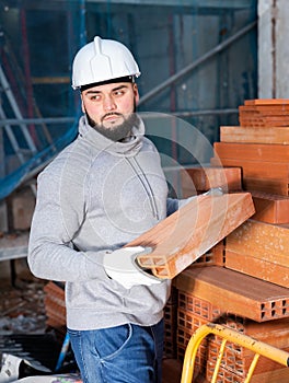 Bricklayer taking red bricks from stack