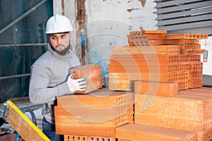 Bricklayer taking red bricks from stack