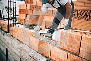 Bricklayer worker installing brick masonry on exterior wall with trowel putty knife