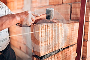 Bricklayer worker installing interior walls with rubber hammer, level and putty knife