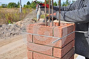 Bricklayer Worker Installing Red Clinker Blocks around Iron Bar