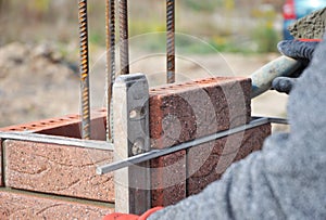 Bricklayer Worker Installing Red Clinker Blocks and Caulking Brick Masonry Joints Exterior Wall with Trowel putty Knife photo