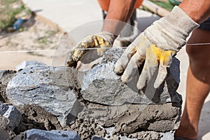 Bricklayer worker in protection yellow gloves installing stones.