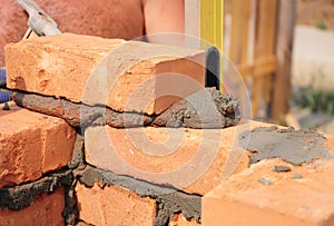 Bricklayer worker installing red blocks and caulking brick masonry joints exterior brick house wall with trowel putty knife