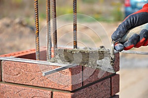 Bricklaying closeup. Bricklayer hand holding a putty knife and building a brick fence column.