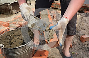 Brickwork and bricklaying: a workman is applying mortar, cement on a brick with a trowel to build a brick wall of a house on a