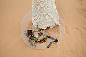 Bridal bouquet lying on the sand next to the bride`s feet.