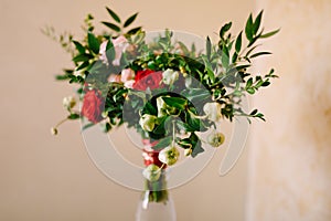 Bridal bouquet of red and pink roses, boxwood branches, not blooming buds of white flowers and red ribbons with brooch