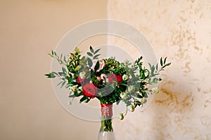 Bridal bouquet of red and pink roses, boxwood branches, not blooming buds of white flowers and red ribbons with brooch
