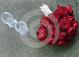 Bridal bouquet with red roses next to wine glasses photo